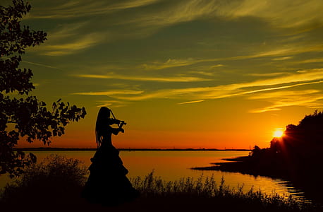 silhouette of woman playing violin beside water during golden hour thumbnail