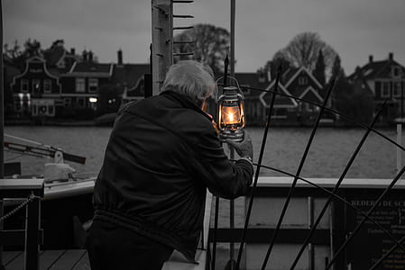 man holding lighted lantern watching over body of water thumbnail