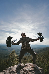 person standing on rock while holding device near trees at daytime thumbnail