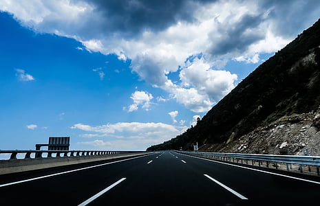 empty highway near body of water and mountain thumbnail