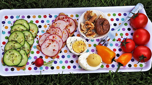 slice of cucumber, ham, and eggs and whole tomatoes and bell peppers on white tray thumbnail