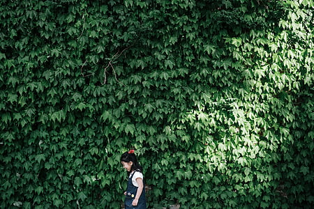 girl standing against green leafed plants thumbnail