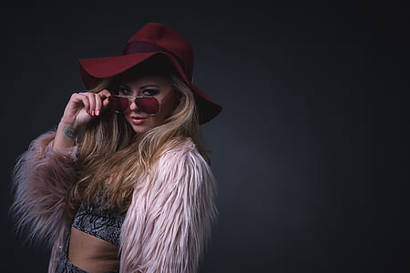 woman holding sunglasses wearing pink fur jacket and red hat thumbnail