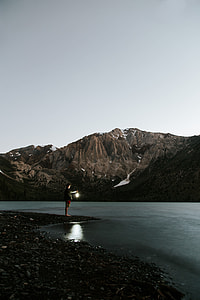 man standing near shore across the brown mountain with cloudy sky during daytime thumbnail