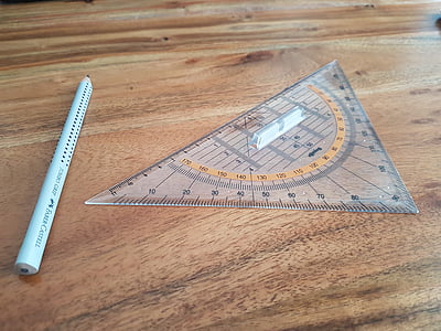 triangular clear plastic ruler beside pensil on brown surface thumbnail