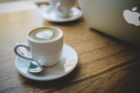 white teacup and saucer beside MacBook on wooden table thumbnail