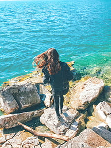 Woman Wearing Denim Jacket Standing on Rock Near Body of Water thumbnail