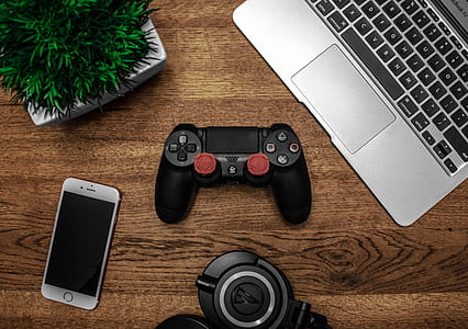 Silver Macbook Beside Black Sony Ps4 Dualshock 4, Silver Iphone 6, and Round Black Keychain on Brown Wooden Table thumbnail