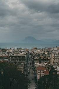 vehicles on road in between buildings under cloudy sky with mountain background thumbnail
