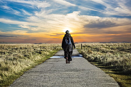 person wearing black jacket walking on path near field thumbnail