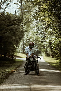 man wearing full-face helmet while riding motorcycle on asphalt roadway between trees during daytime thumbnail