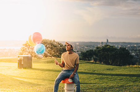 man holding three assorted-color balloon on green grass field thumbnail