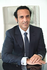 smiling man wearing black suit jacket sitting on chair thumbnail