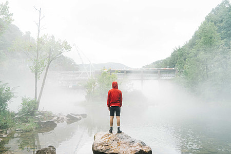 person in red hoodie standing on gray rock surround by body of water thumbnail