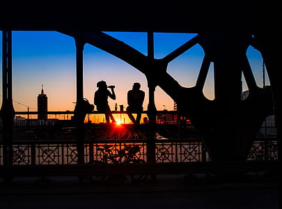 silhouette of man and woman sitting on railing during golden hour thumbnail