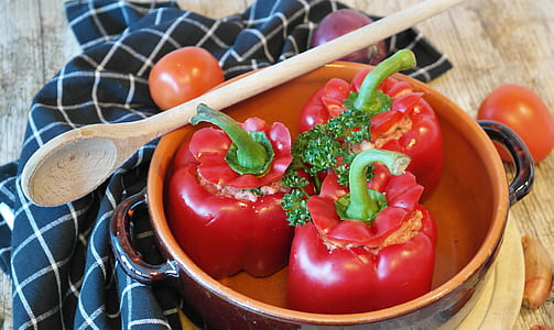 three red bell peppers in bowl with wooden spoon on table thumbnail