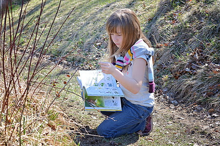 girl writing down on book while kneeling on grass thumbnail