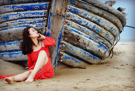 woman wearing red cold-shoulder dress leaning on blue wooden boat thumbnail