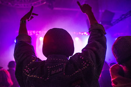 Back of Man Raising Hands Inside Room Full of People With Purple Lights thumbnail