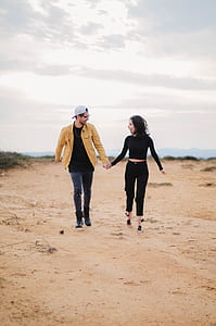 man and woman holding hands while walking on sand thumbnail