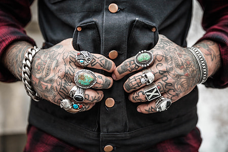 person with arm tattoo and silver-colored rings wearing jacket thumbnail