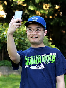 man in blue Seattle Seahawks crew-neck shirt holding smartphone thumbnail