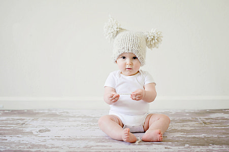 baby wearing white onesie with beige bubble cap sitting on the floor thumbnail