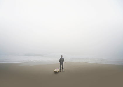 person standing at shoreline near white surfboard thumbnail