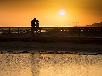 man and woman standing on wooden dock during sunset thumbnail