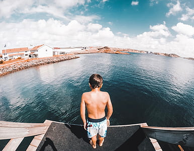 boy wearing blue shorts near body of water under white clouds during daytime thumbnail