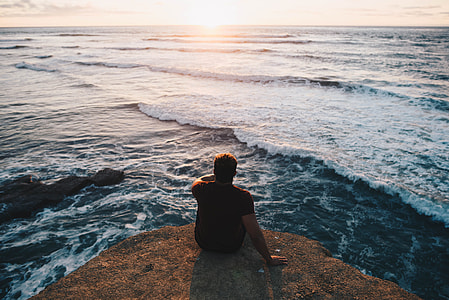 man sitting on rock near sea thumbnail
