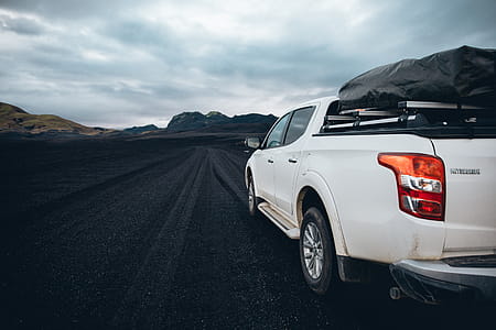 Side view of a white pick-up truck passing on a highway with overcast weather in the background thumbnail