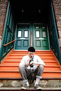 man sitting on stairs in front of green doors during daytime thumbnail