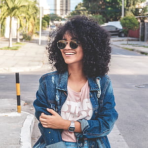 woman with curly hair wearing blue jacket and sunglasses smiling thumbnail
