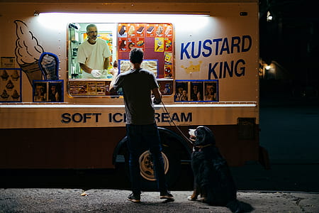 person wearing gray shirt holding dog leash while reaching for ice cream from ice cream truck thumbnail
