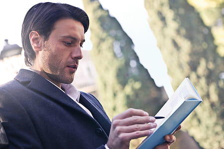 A young caucasian man wearing a grey coat writing on a notebook in the park thumbnail