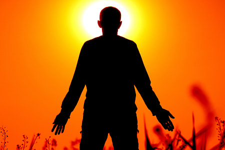 silhouette of person standing on grass field in front of orange sunset thumbnail