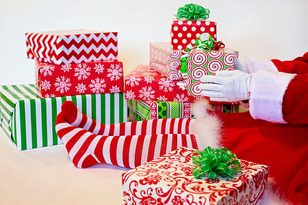 person wearing red and white santa dress sitting down near gifts holding green and red present thumbnail