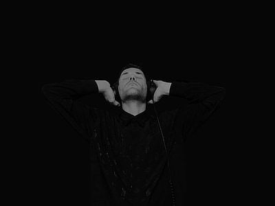 grayscale photo of man wearing long-sleeved collared shirt and corded headphones thumbnail