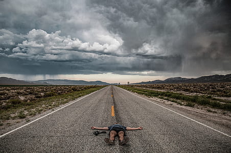 person lying on grey asphalt road under the cloudy sky thumbnail