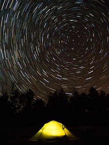 long exposure stars photography of yellow tent behind trees thumbnail