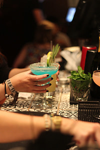 selective focus photography of person's right hand holding blue margarita glass in front of white and black table thumbnail
