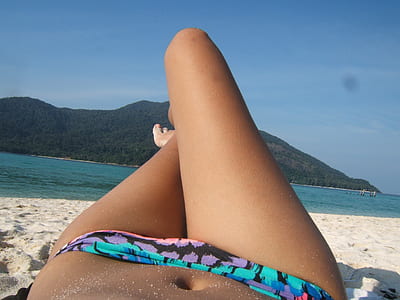 woman wearing blue and multicolored bikini bottom lying on white sand near blue sea at daytime thumbnail