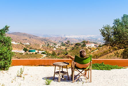 Man Sitting on Green Chair Near Trees and Mountain Under Blue Sky at Daytime thumbnail