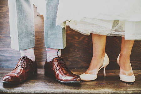 person wearing gray trousers and brown leather dress shoes beside person wearing white pumps and white skirt over brown wooden surface thumbnail