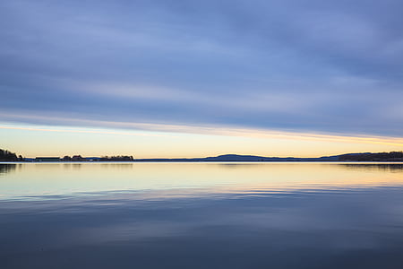 calm body of water bear mountains under white sky during golden hour thumbnail