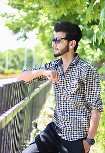 man leaning on fence next to green tree thumbnail