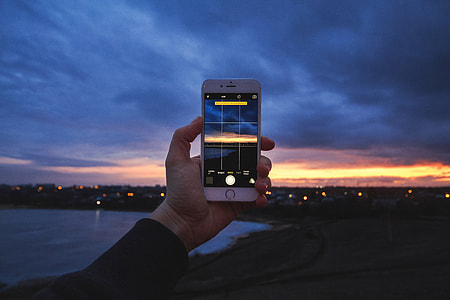 Man photographer using his mobile iPhone smartphone camera at sunset thumbnail