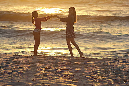 woman and girl holding hands while standing on shore thumbnail