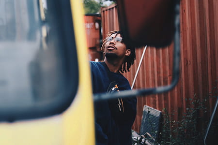 man in black jacket standing nearing yellow vehicle looking up thumbnail